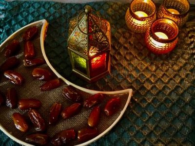 A half moon shaped tray with dates and an oriental lamp with three little tea light holder on a green mat for Ramadan decoration